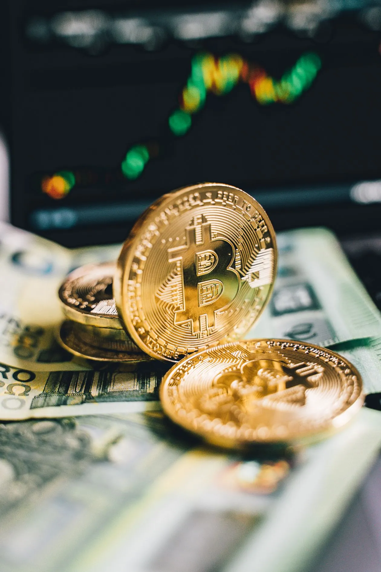 Physical Bitcoin coins resting on banknotes in front of a price chart
